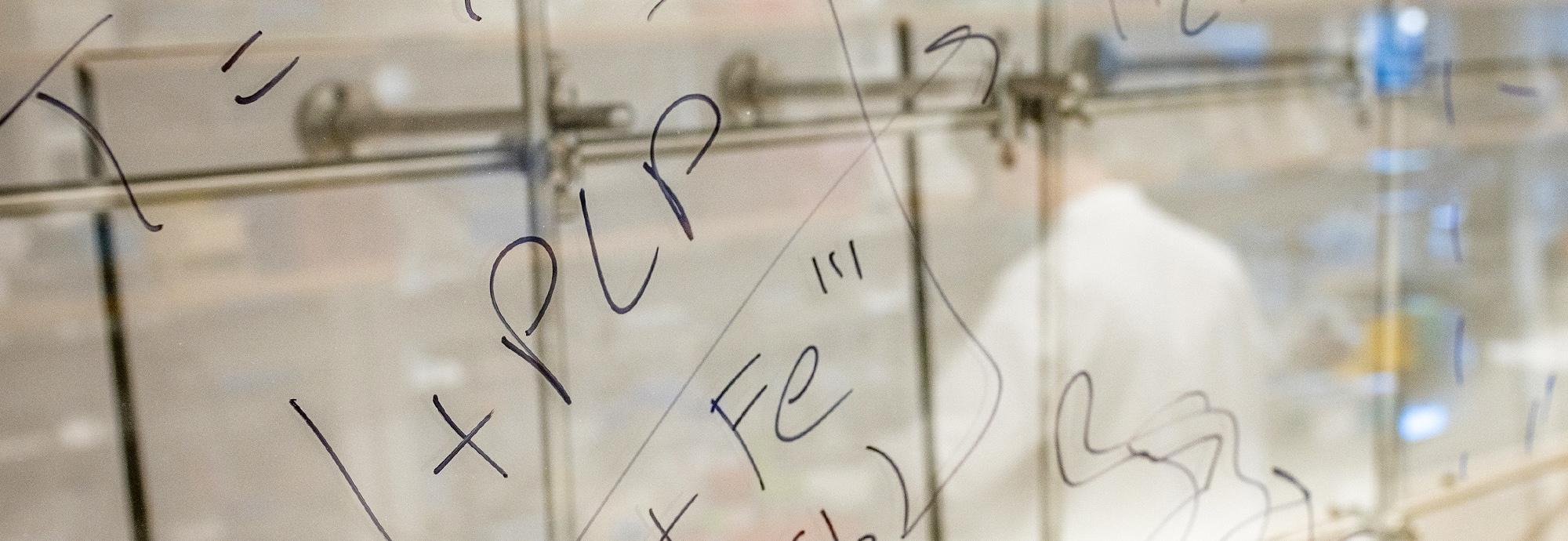 Writing on a whiteboard that is reflecting a person in a lab