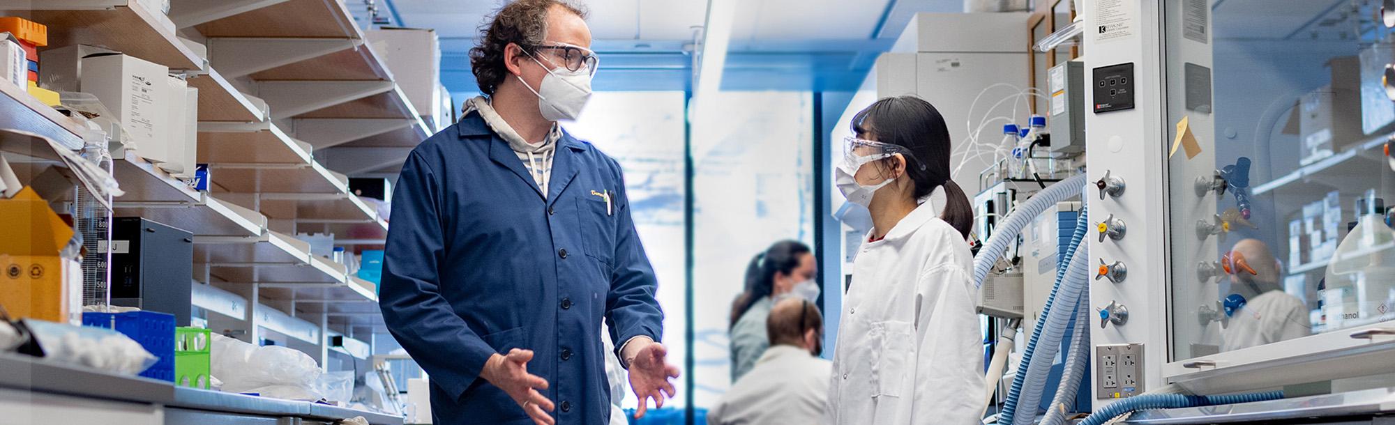 Two people wearing masks and talking in a lab